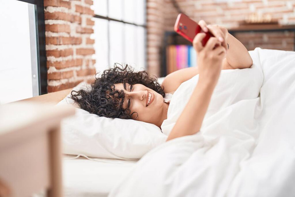 Jovem mulher do Oriente Médio usando smartphone deitado na cama no quarto - Foto, Imagem
