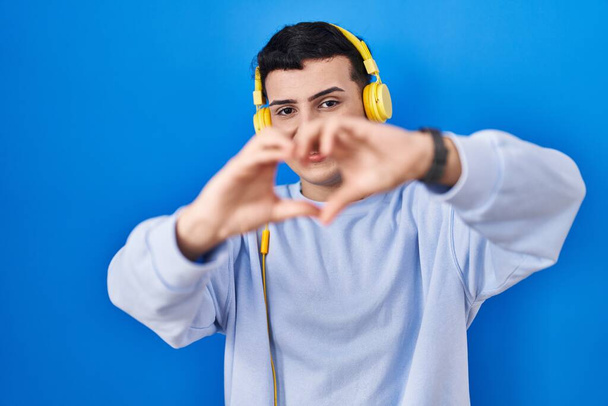Non binary person listening to music using headphones smiling in love doing heart symbol shape with hands. romantic concept.  - Foto, immagini