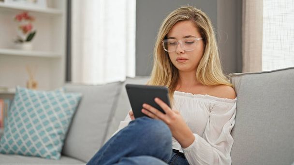 Mujer rubia joven con gafas usando touchpad en casa - Foto, Imagen