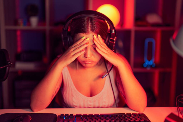 Молодая блондинка, играющая в видеоигры в наушниках с грустным лицом, закрывающим лицо руками во время плача. депрессия.  - Фото, изображение