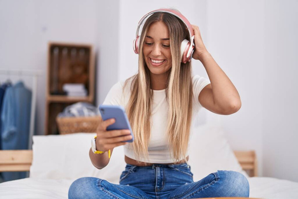 Young beautiful hispanic woman listening to music sitting on bed at bedroom - Foto, afbeelding