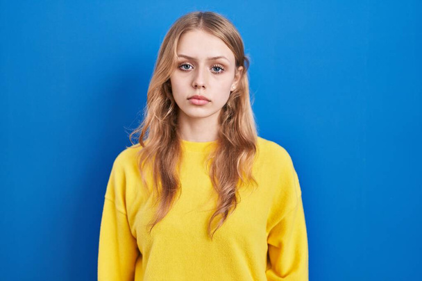 Young caucasian woman standing over blue background relaxed with serious expression on face. simple and natural looking at the camera.  - Fotoğraf, Görsel