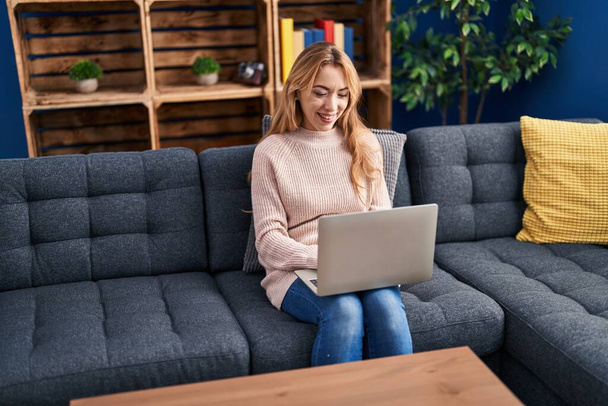 Молодая женщина с ноутбуком сидит на диване дома - Фото, изображение