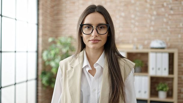 Young beautiful hispanic woman business worker standing with relaxed expression at office - Foto, afbeelding