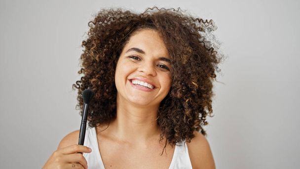 Giovane bella donna ispanica sorridente fiducioso tenendo trucco pennello su sfondo bianco isolato - Foto, immagini