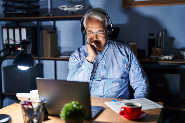 Latynoski starszy mężczyzna noszący słuchawki agenta call center w nocy, z uśmiechem na twarzy, z skrzyżowanymi ramionami i ręką podniesioną na brodzie. pozytywne myślenie.  - Zdjęcie, obraz