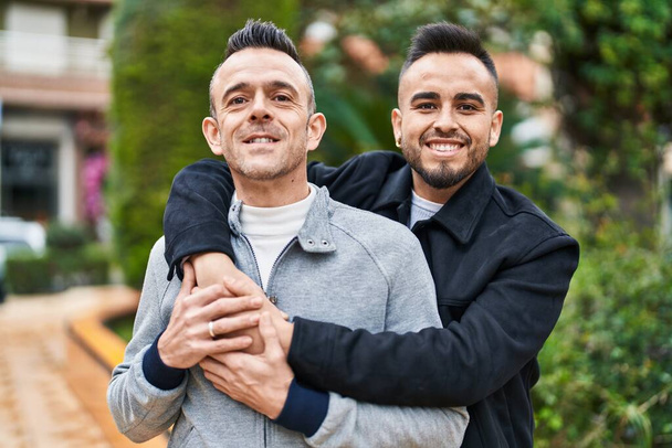Zwei Männer lächeln selbstbewusst und umarmen sich im Park - Foto, Bild
