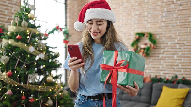 Jonge mooie Spaanse vrouw met behulp van smartphone vieren kerst thuis - Foto, afbeelding