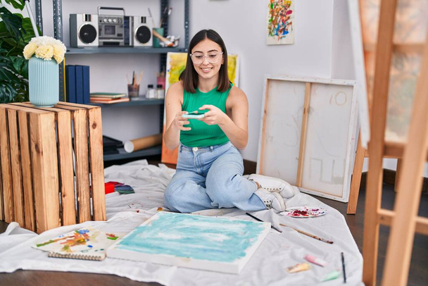 Genç İspanyol kadın sanatçı, resim stüdyosunda akıllı telefon ile fotoğraf çekiyor. - Fotoğraf, Görsel