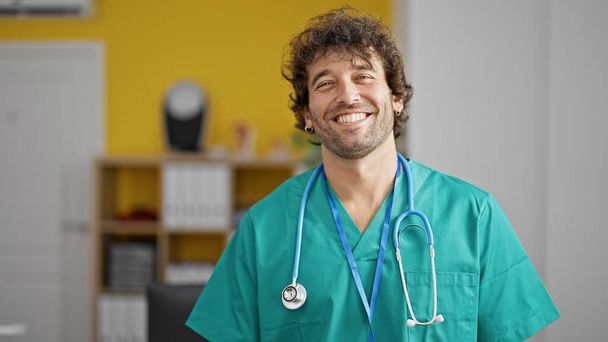Jovem hispânico homem médico sorrindo confiante em pé na clínica - Foto, Imagem