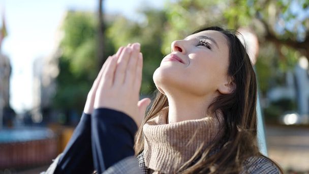 Beautiful hispanic woman praying with closed eyes at park - 写真・画像