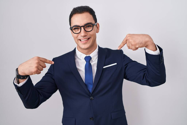 Joven hombre hispano vistiendo traje y corbata que mira confiado con sonrisa en la cara, señalándose con los dedos orgullosos y felices.  - Foto, imagen