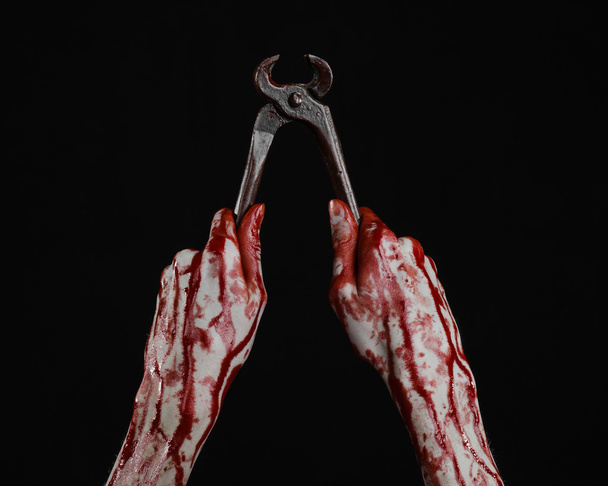 Halloween theme: bloody hand holding a pliers on a black background - 写真・画像