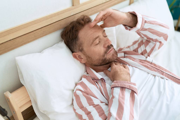 Mann mittleren Alters leidet unter Kopfschmerzen, wenn er im Schlafzimmer im Bett liegt - Foto, Bild