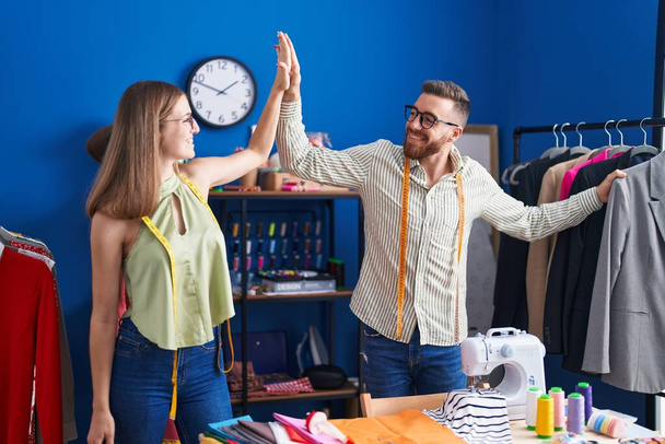 Man and woman tailors high five with hands raised up at clothing factory - 写真・画像