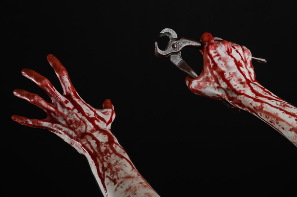 Halloween theme: bloody hand holding a pliers on a black background - Photo, image