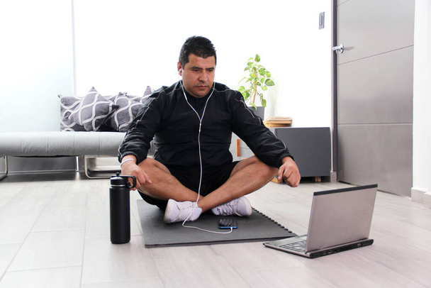 Donkerharige 40-jarige Latino-man beoefent yoga in zijn woonkamer met een online instructeur voor een mentale, spirituele en fysieke discipline - Foto, afbeelding