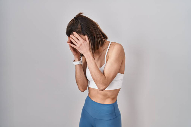 Іспаномовна жінка в спортивному одязі над ізольованим тлом з сумним виразом, що покриває обличчя руками під час плачу. концепція депресії.  - Фото, зображення