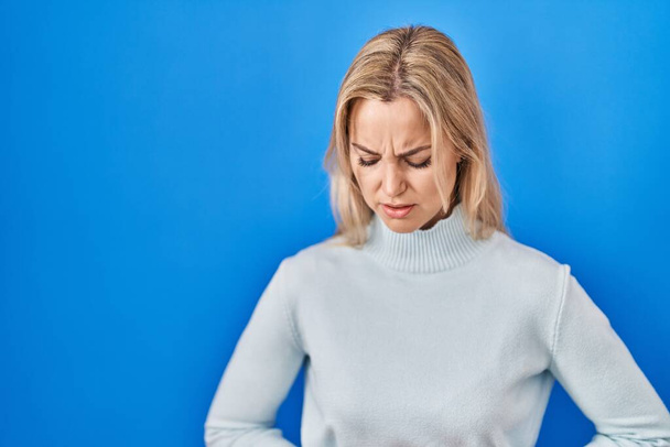 Молодая белая женщина стоит на синем фоне с рукой на животе, потому что тошнота, болезненное заболевание чувствует себя нездоровым. Концепция.  - Фото, изображение