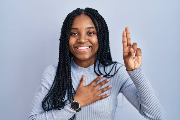 African american woman standing over blue background smiling swearing with hand on chest and fingers up, making a loyalty promise oath  - Fotografie, Obrázek