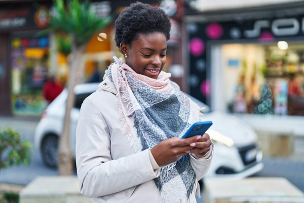 Afro-Amerikalı kadın sokakta akıllı telefon kullanarak kendine güveniyor. - Fotoğraf, Görsel