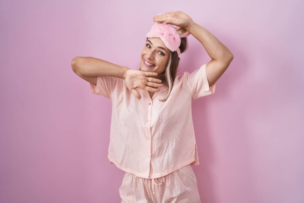 Blonde caucasian woman wearing sleep mask and pajama smiling cheerful playing peek a boo with hands showing face. surprised and exited  - Fotoğraf, Görsel