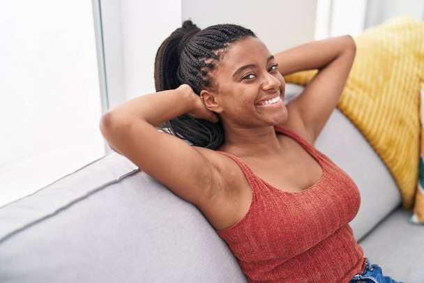 Afričanky americká žena uvolněná s rukama na hlavě sedí na pohovce doma - Fotografie, Obrázek
