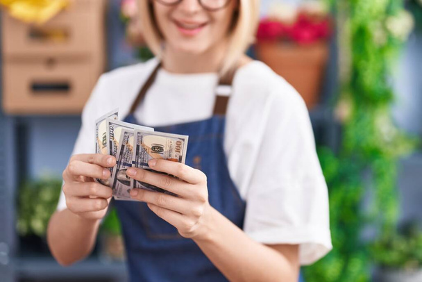Young blonde woman florist counting dollars at florist shop - Photo, Image