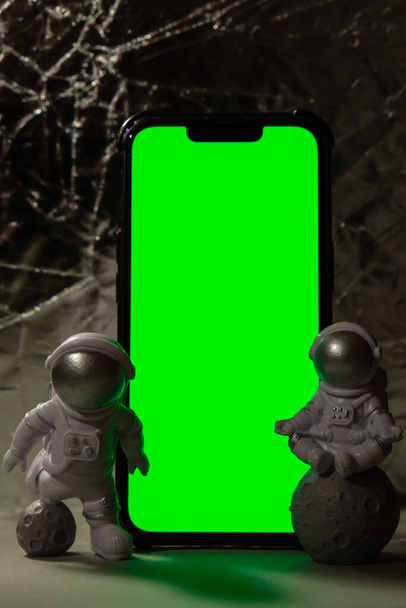 あなたの広告のための携帯電話のクロマキーグリーンスクリーンを持つプラスチック製のおもちゃのフィギュア宇宙飛行士コピースペース。地球旅行、民間の宇宙飛行のうちの概念。宇宙飛行士 - 写真・画像