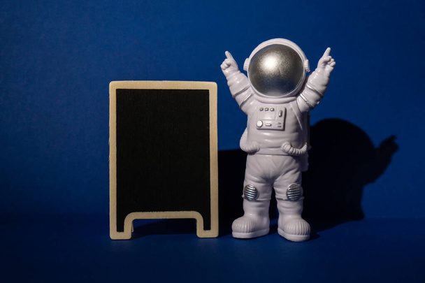 Plastic toy astronaut with blackboard template mock up for your text on colorful blue background Copy space. Concept of out of earth travel, private spaceman commercial flights. Space missions and - Fotó, kép