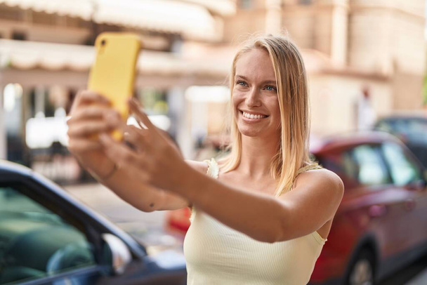 Young blonde woman smiling confident making selfie by the smartphone at street - 写真・画像