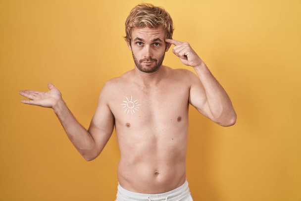 Λευκός άνδρας στέκεται γυμνός φορώντας αντηλιακό μπερδεμένος και ενοχλημένος με ανοιχτή παλάμη που δείχνει το χώρο των αντιγράφων και δείχνει το δάχτυλο στο μέτωπο. Σκέψου το..  - Φωτογραφία, εικόνα