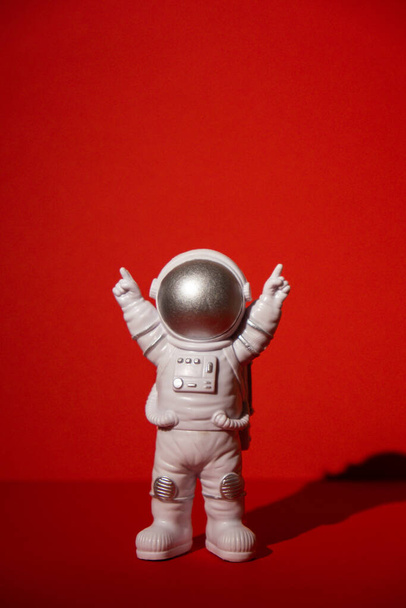 Plastic toy astronaut on colorful red background Copy space. Concept of out of earth travel, private spaceman commercial flights. Space missions and Sustainability - Photo, Image