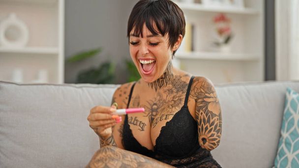 Mulher hispânica com braço amputado vestindo lingerie olhando teste de gravidez sorrindo em casa - Foto, Imagem