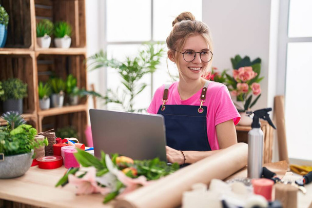 Young blonde woman florist smiling confident using laptop at flower shop - Foto, afbeelding