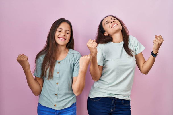 Young mother and daughter standing over pink background celebrating surprised and amazed for success with arms raised and eyes closed. winner concept.  - Foto, imagen