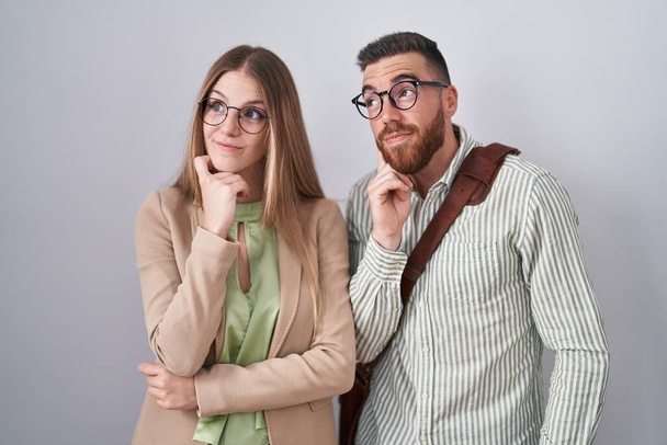 Young couple standing over white background with hand on chin thinking about question, pensive expression. smiling with thoughtful face. doubt concept.  - Photo, Image