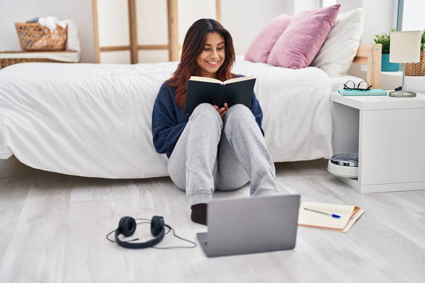 Young hispanic woman studying sitting on floor at bedroom - Foto, Imagem