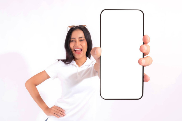 Красивая азиатская брюнетка милая девушка в белой рубашке, взволнованная удивленная девушка показывает большой смартфон с пустым экраном, белый экран изолирован на белом фоне, Показать макет изображения - Фото, изображение