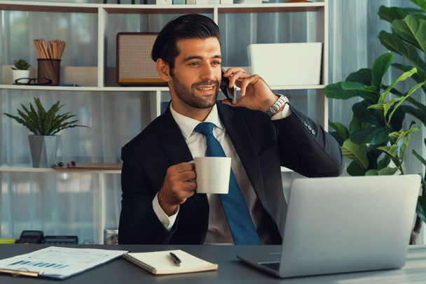 Empresário diligente ocupado conversando no telefonema com os clientes enquanto trabalhava com laptop em seu escritório como conceito de estilo de vida moderno trabalhador de escritório com telefone celular. Fervente - Foto, Imagem