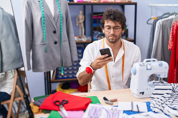 Young hispanic man tailor using smartphone at clothing factory - Photo, Image