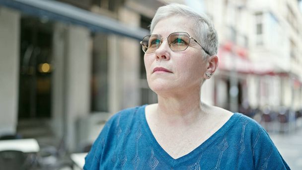 Grauhaarige Frau mittleren Alters blickt mit ernstem Gesichtsausdruck auf die Straße - Foto, Bild