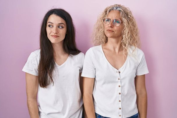Mother and daughter standing together over pink background smiling looking to the side and staring away thinking.  - Photo, Image