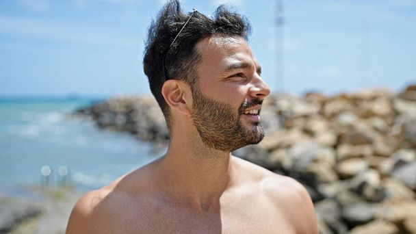Fiatal spanyol férfi turista mosolyog magabiztos félmeztelen a strandon - Fotó, kép