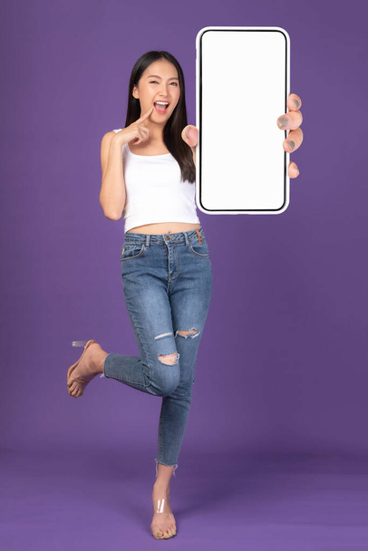 Retrato de foto de cuerpo completo de una hermosa mujer joven asiática, Muchacha sorprendida emocionada mostrando un gran teléfono inteligente con pantalla en blanco, pantalla blanca aislada sobre fondo púrpura, Imagen falsa - Foto, Imagen
