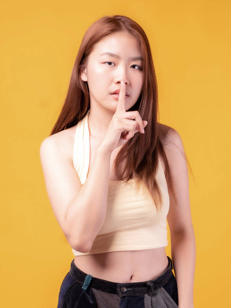 Hymyilevän kauniin aasialaisen nuoren naisen muotokuva tuntuu vakavalta Huono mieliala vihainen pitää sormensa suussaan, mikä tekee hiljaisuuden eleestä eristetyn keltaisella taustalla. - Valokuva, kuva