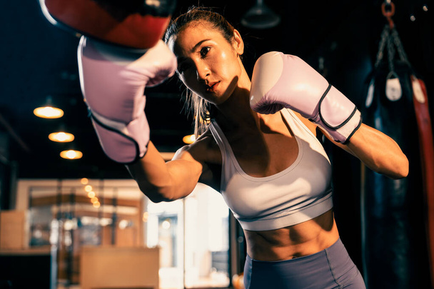 Asian female Muay Thai boxer punching in fierce boxing training session, delivering strike to her sparring trainer wearing punching mitts, showcasing Muay Thai boxing technique and skill. Impetus - Foto, Bild