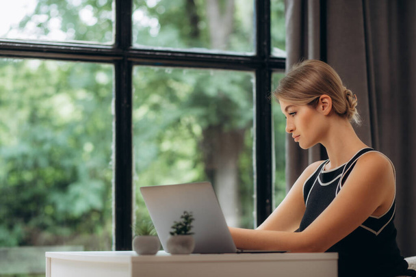 Krásná mladá žena pracující s laptopem na útulné pohovce v blízkosti velkého okna. - Fotografie, Obrázek