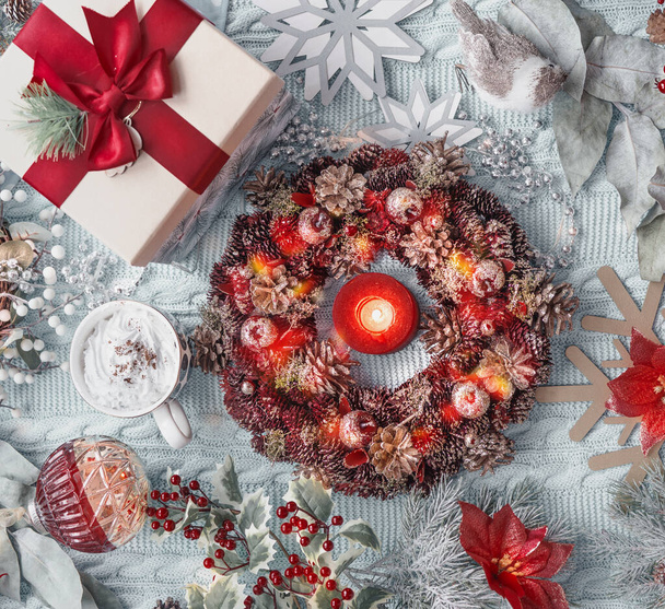 Christmas concept: advent wreath, present, hot chocolate in mug, Christmas flower, snowflakes, Christmas balls, and holly on light blue textile background. Top view - 写真・画像