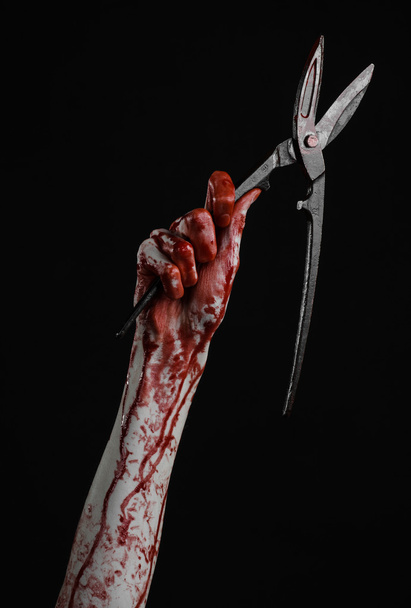 Halloween theme: bloody hand holding a big old bloody scissors on a black background - Fotó, kép